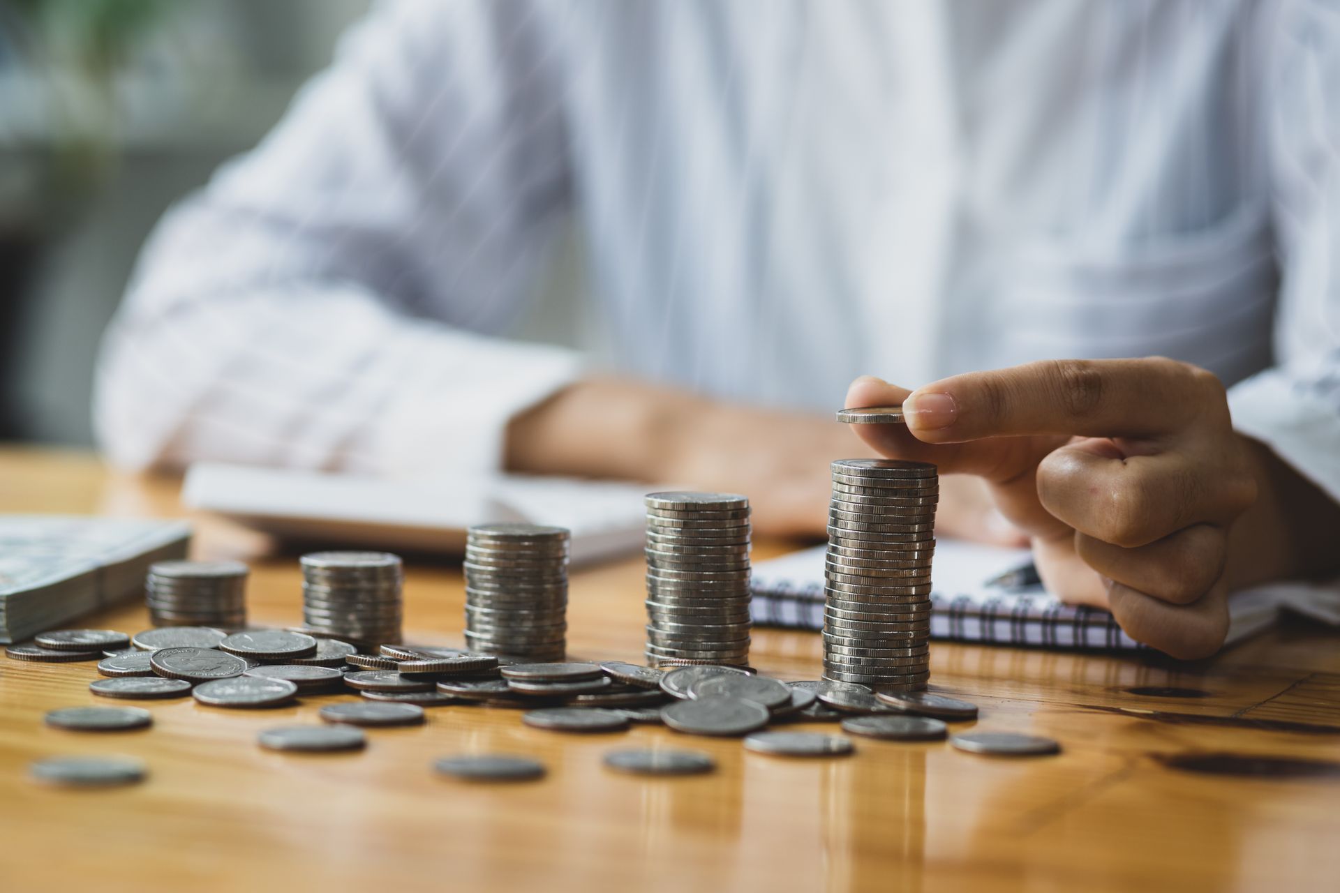 Photograph of a person sat at a table as they count coins, stacking them carefully.