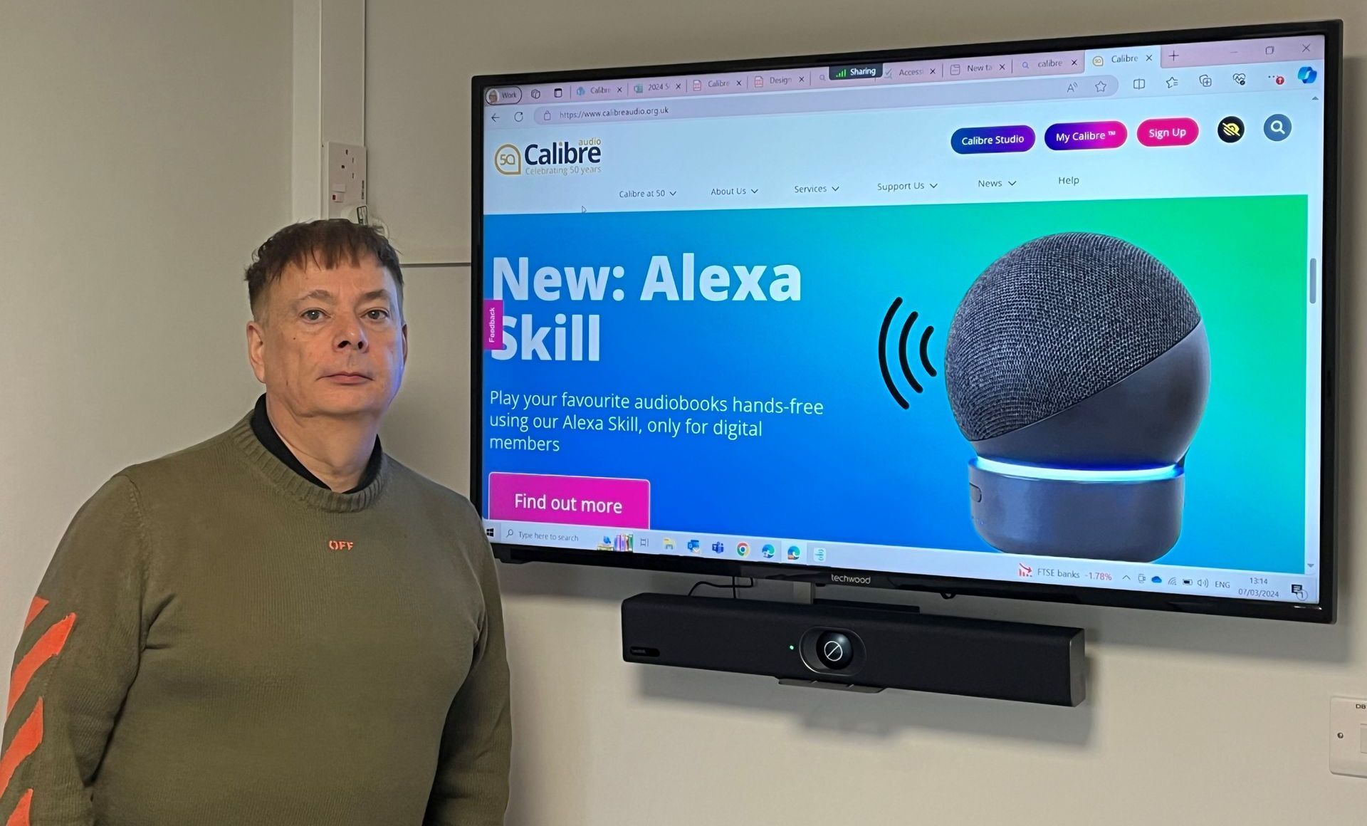 A photo of Calibre's Anthony Kemp stood by a display highlighting Calibre's New Alexa skill.