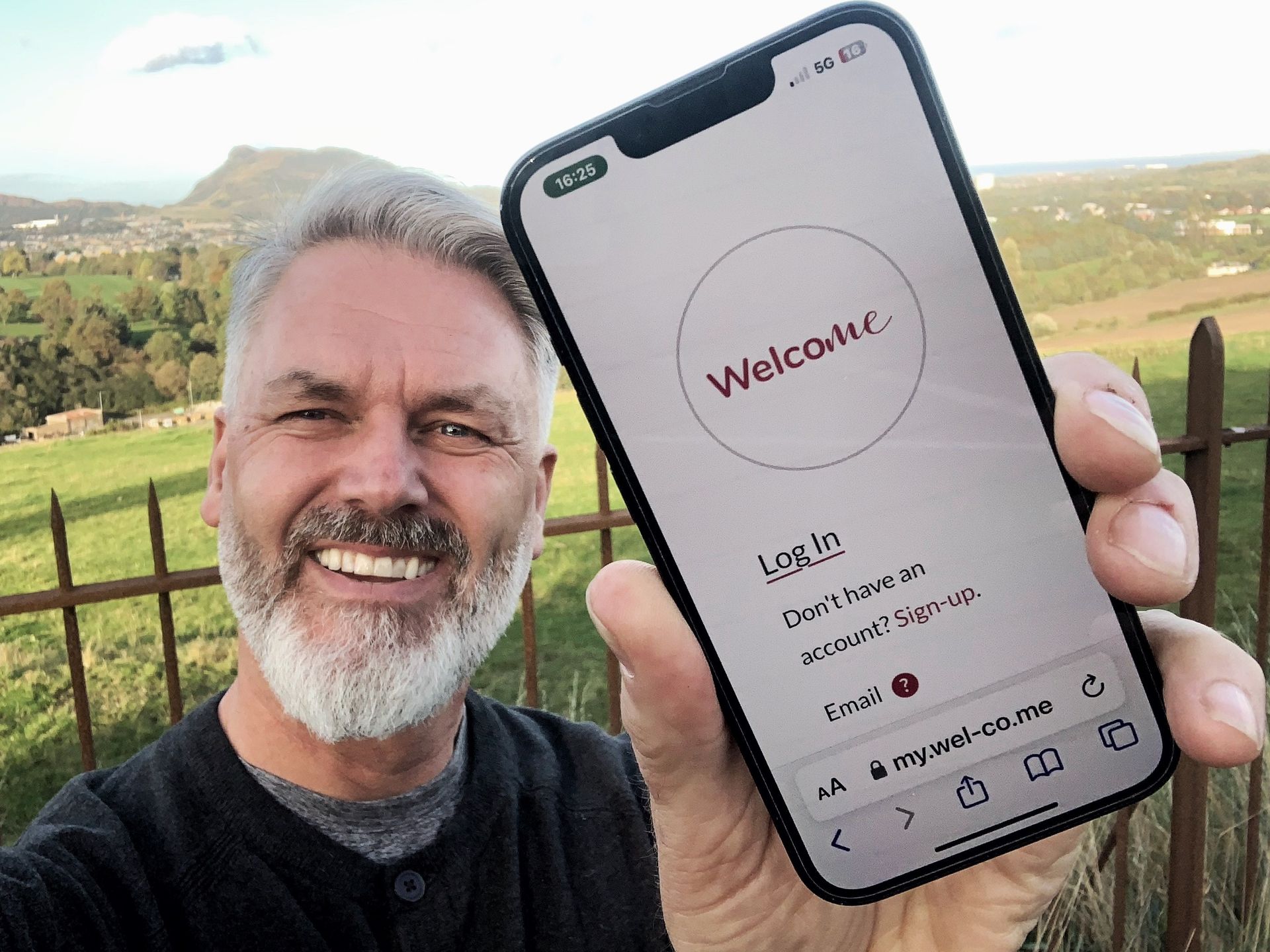 A photo of WelcoMe founder Gavin Neate holding a phone showing the WelcoMe app  in the countryside