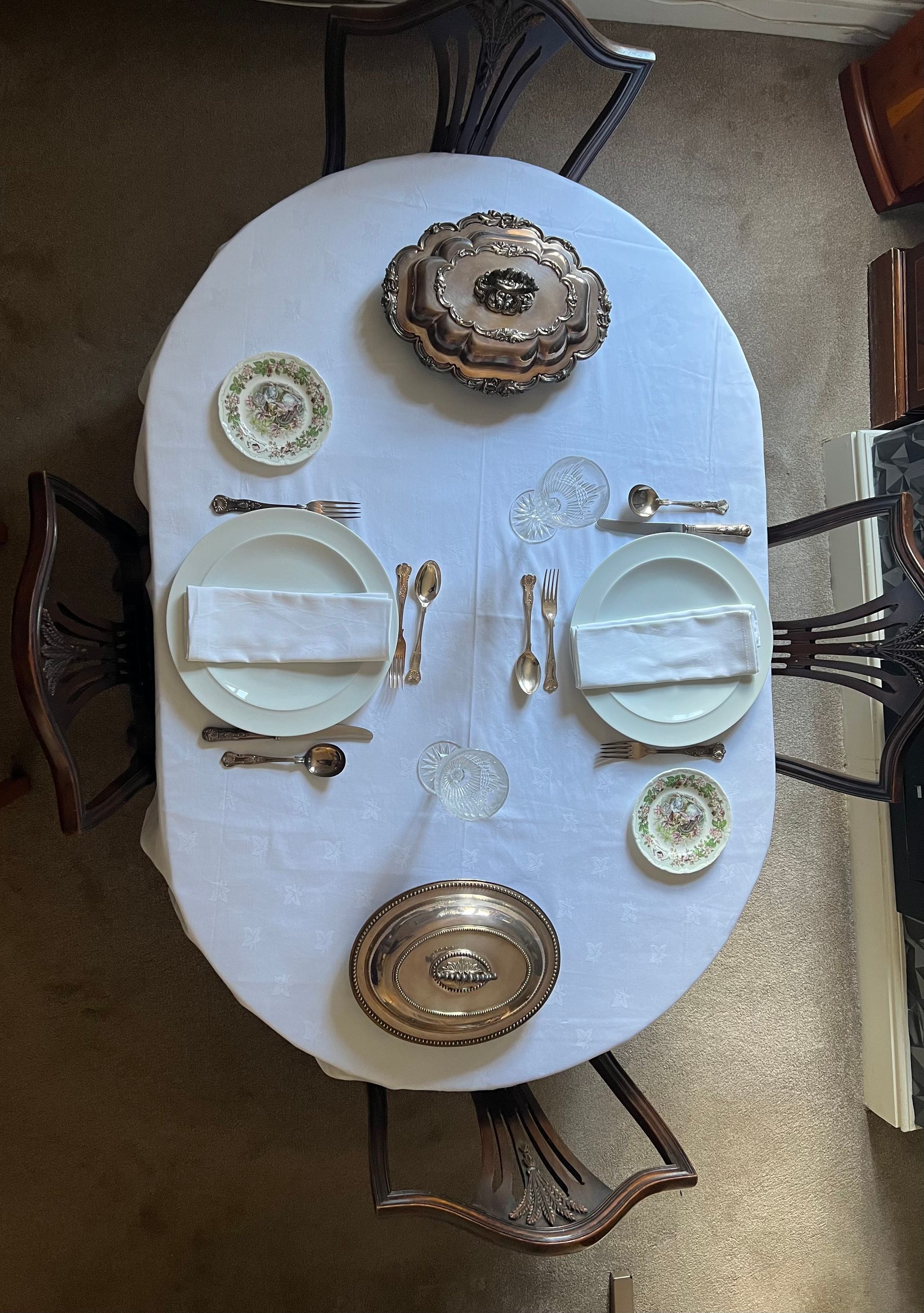 Aerial shot of a neat dining table with subtle, ornate place settings and a crisp, white tablecloth.