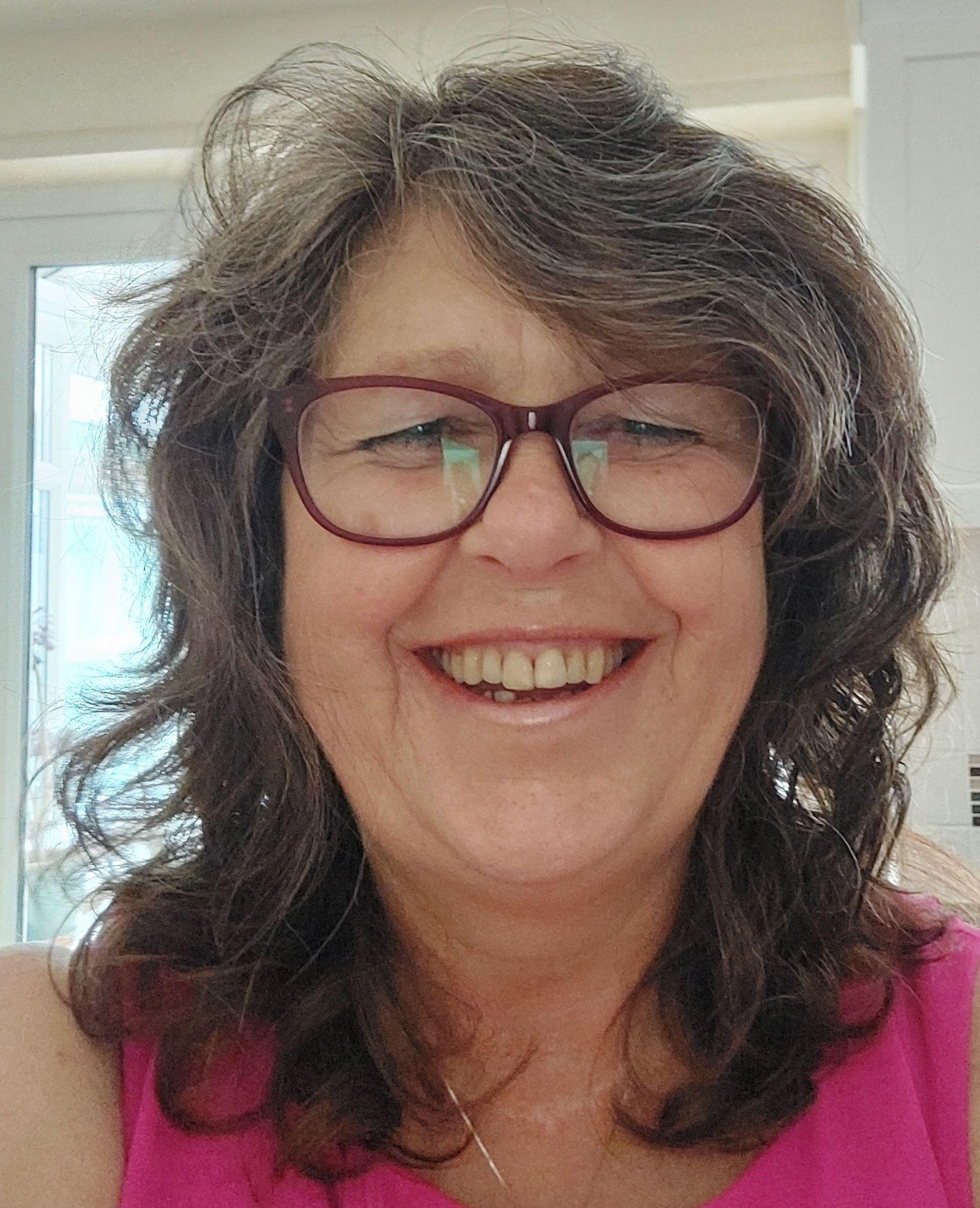 A portrait photograph of Angela Peak, smiling cheerfully towards the camera.