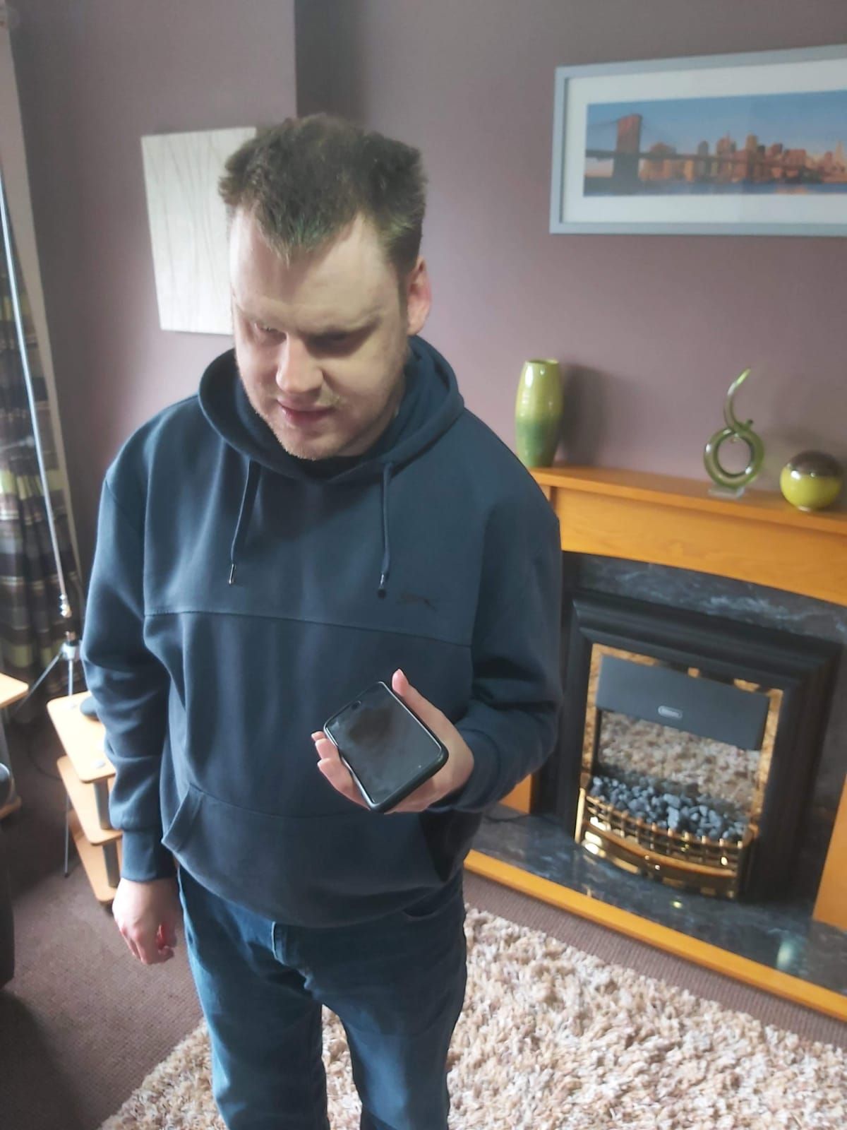 A photograph of Martin Rhodes, stood in a living room while using his iPhone.