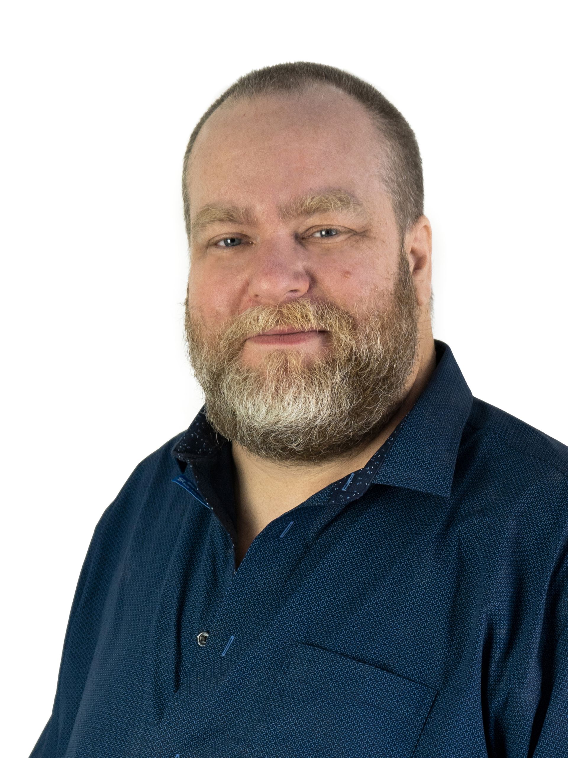 A photograph of Mathieu Paquette, a middle aged man with a kind face, full beard, and a shirt worn with its top three buttons undone.