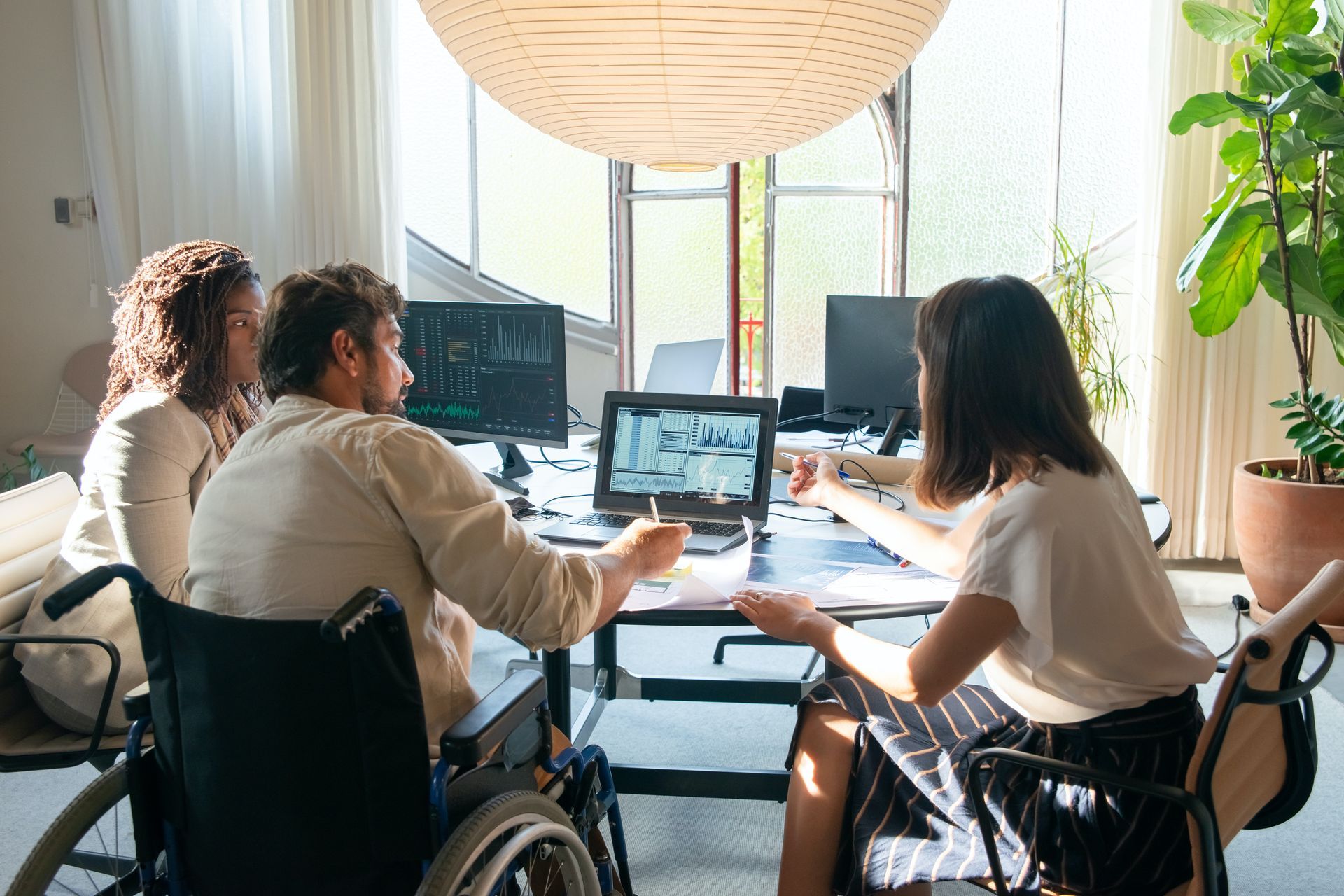 A group of colleagues gather around a table. The table is at an accessible height for the man who is in a wheelchair. 