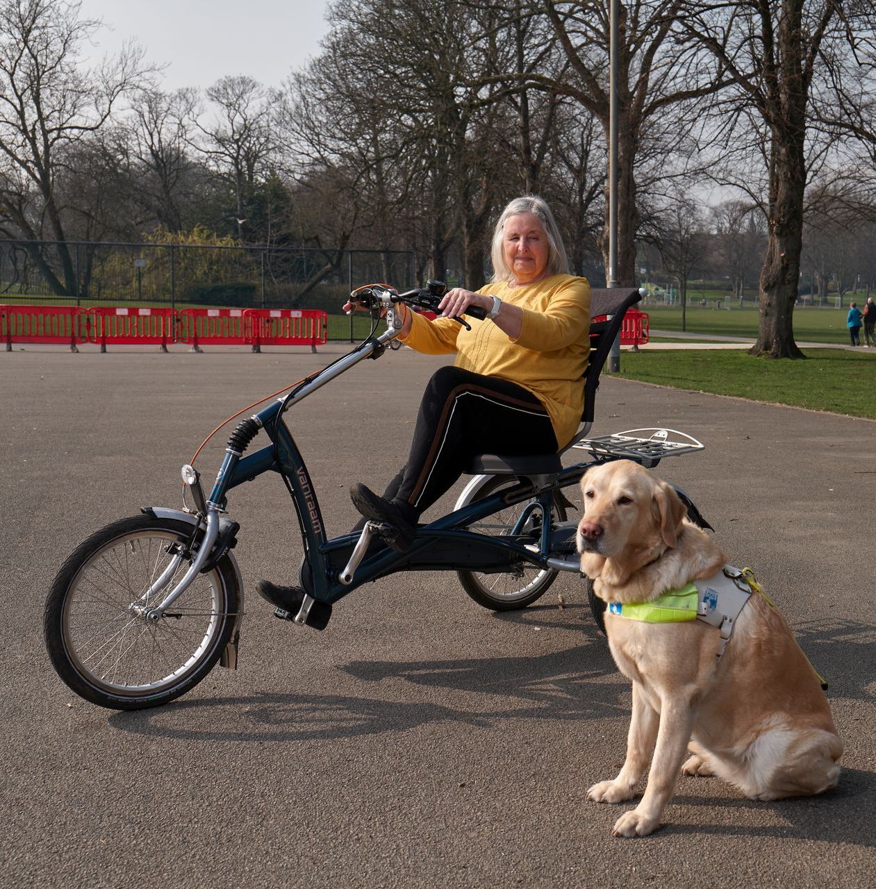 An elderly woman rides a disability bike, accompanied by her guide dog.