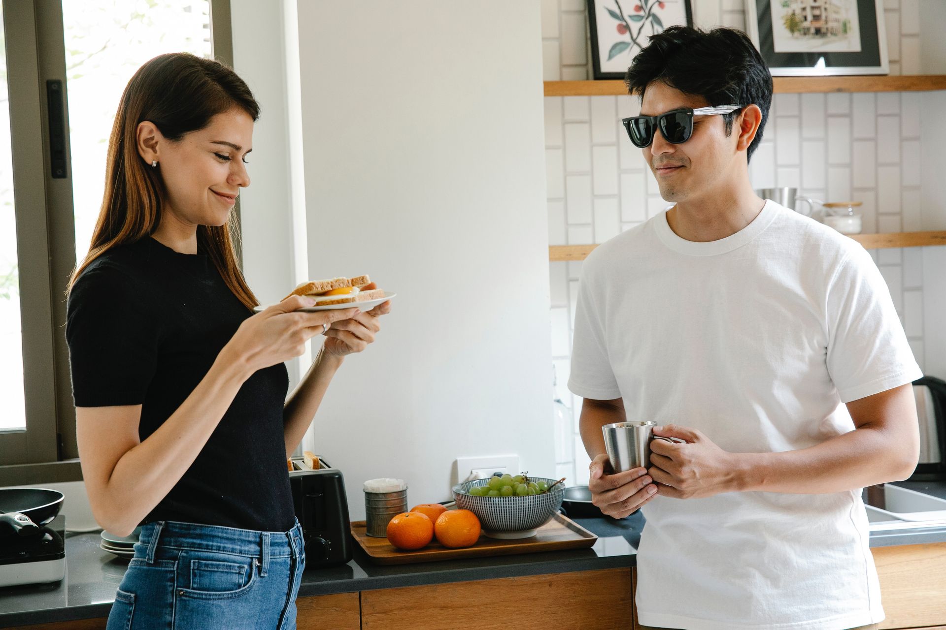 A young man with sight loss nurses a cup of coffee as a young woman accepts a toasted egg sandwich.