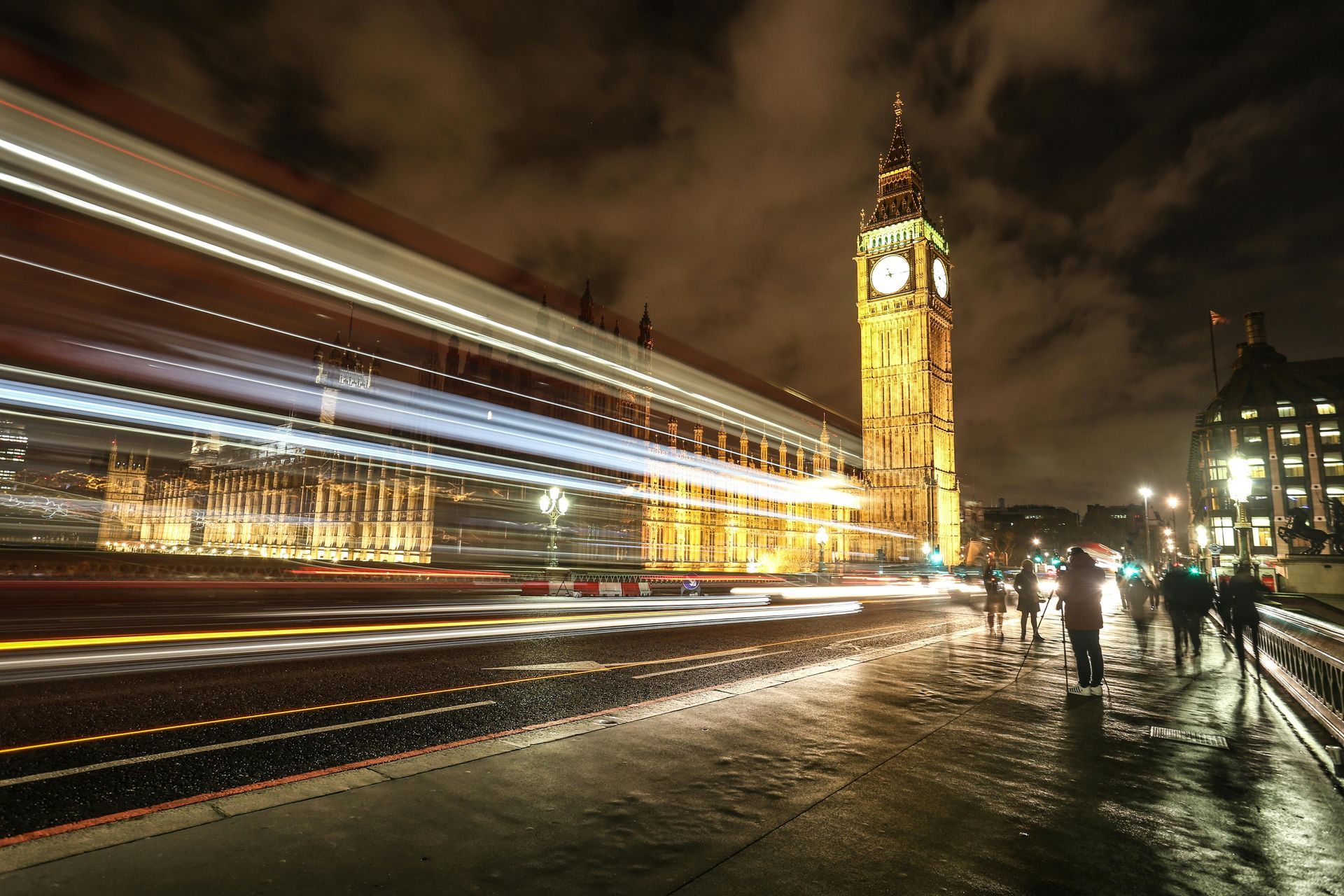 Night time photograph of traffic and pedestrians bustling across Westminster Bridge with the Houses of Parliament illuminated in the background.