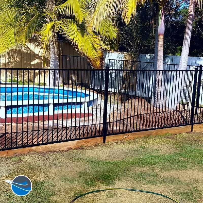 A Black Fence Surrounds a Swimming Pool With Palm Trees in the Background — Strike Fencing & Gates in Bateau Bay, NSW