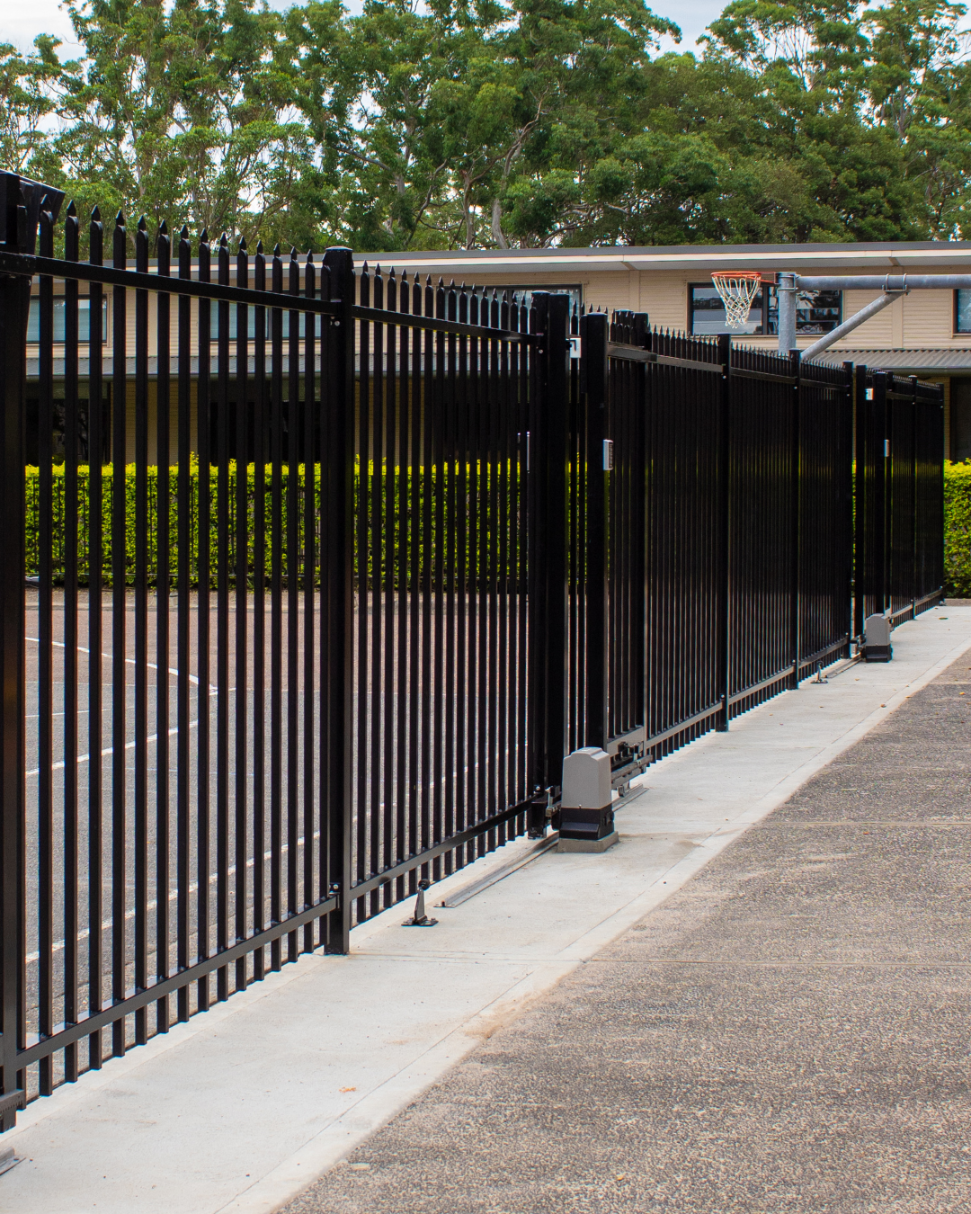 A Black Fence Surrounds a Parking Lot with Trees in The Background — Strike Fencing & Gates in Woy Woy, NSW