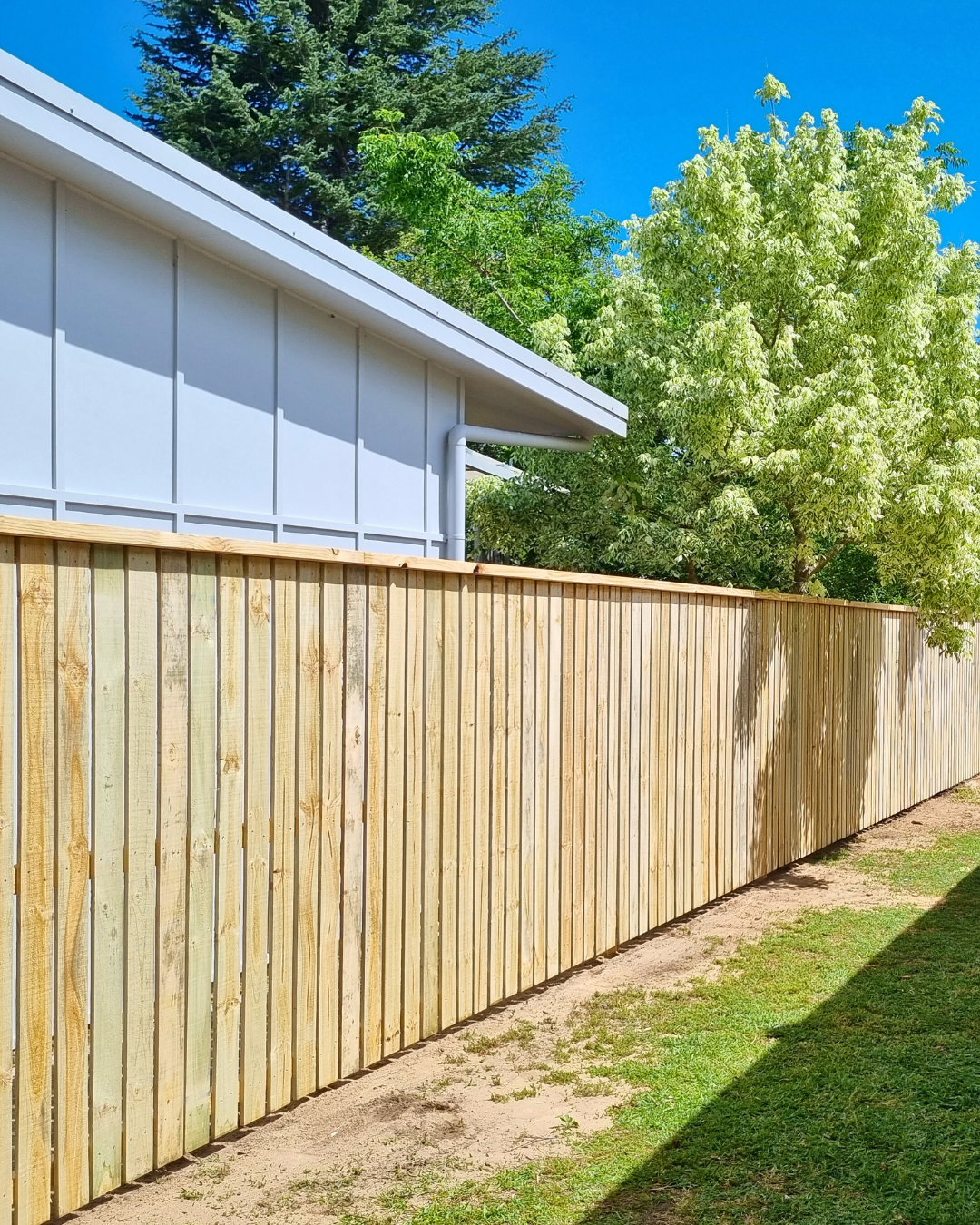 Wooden Fence Beside A Building With A White Wall And Green Trees, Sunny Day