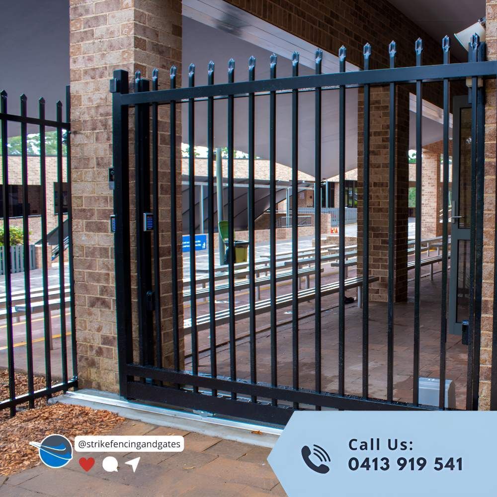 A Black Wrought Iron Gate With a Brick Building in the Background — Strike Fencing & Gates in Terrigal, NSW