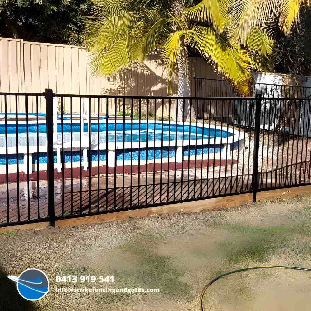 A Black Metal Fence Surrounds a Swimming Pool With Palm Trees in the Background — Strike Fencing & Gates in Umina, NSW