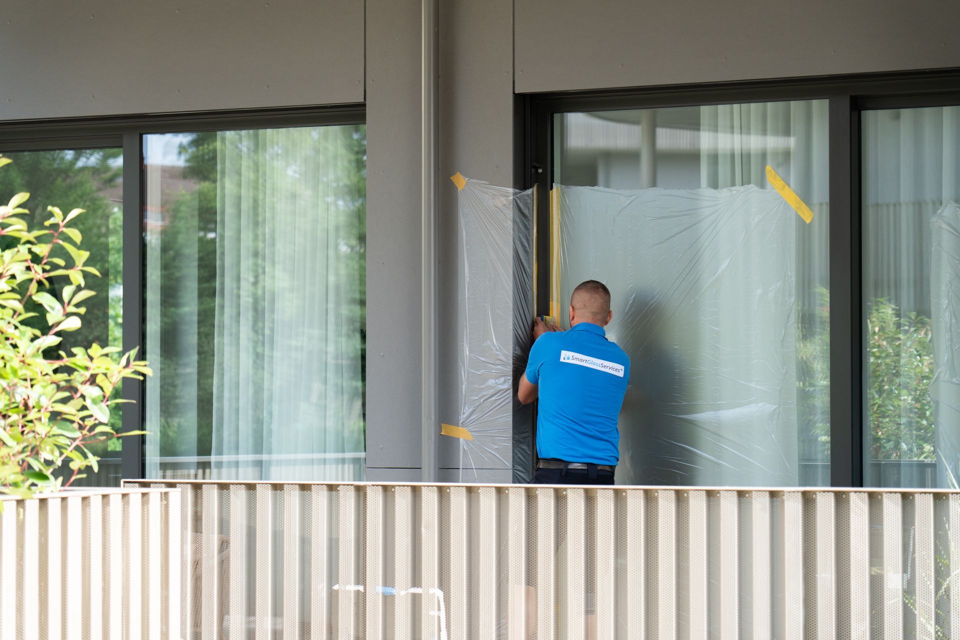 Ein Mann in einem blauen Hemd putzt ein Fenster auf einem Balkon.