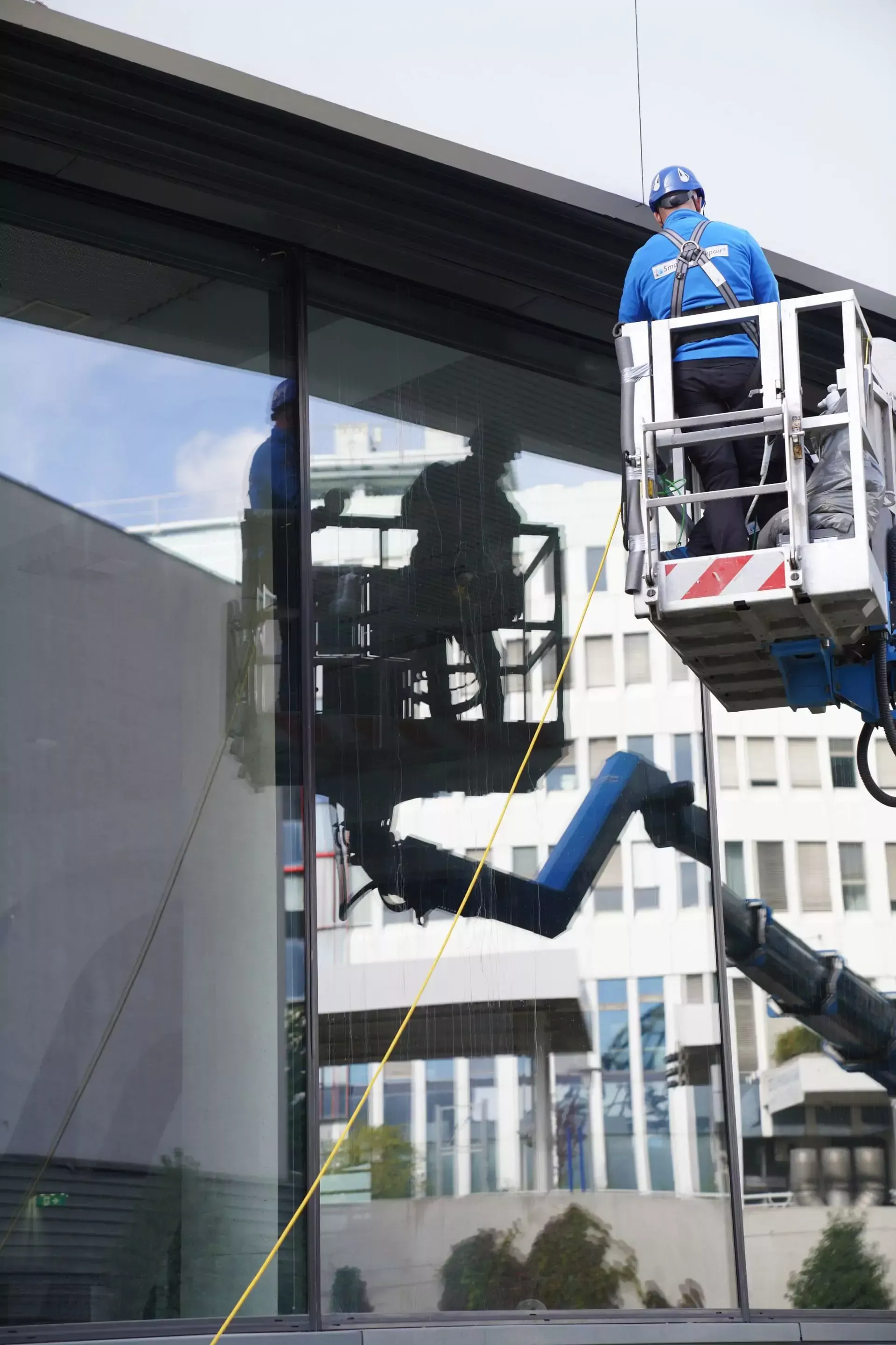 Ein Mann in einem blauen Hemd putzt mit einem Kran ein Fenster.