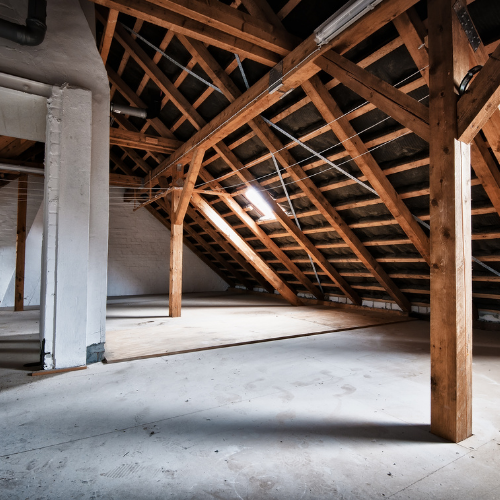 Empty attic with wooden beams, concrete floor, and natural light.