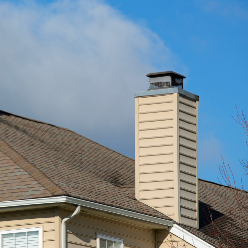 Tan chimney extending from a brown roof against a blue sky with clouds.