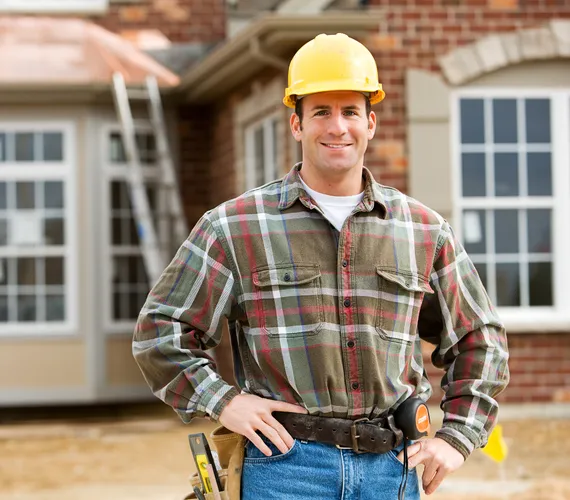 A man wearing a hard hat is standing in front of a house