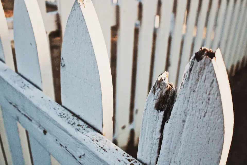 A close up of a white picket fence with a broken post.