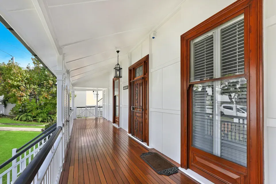 A long wooden porch with shutters on the windows of a white house.