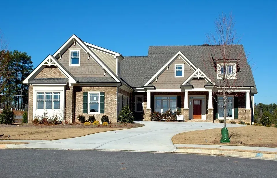 A large house with a concrete driveway and a tree in front of it