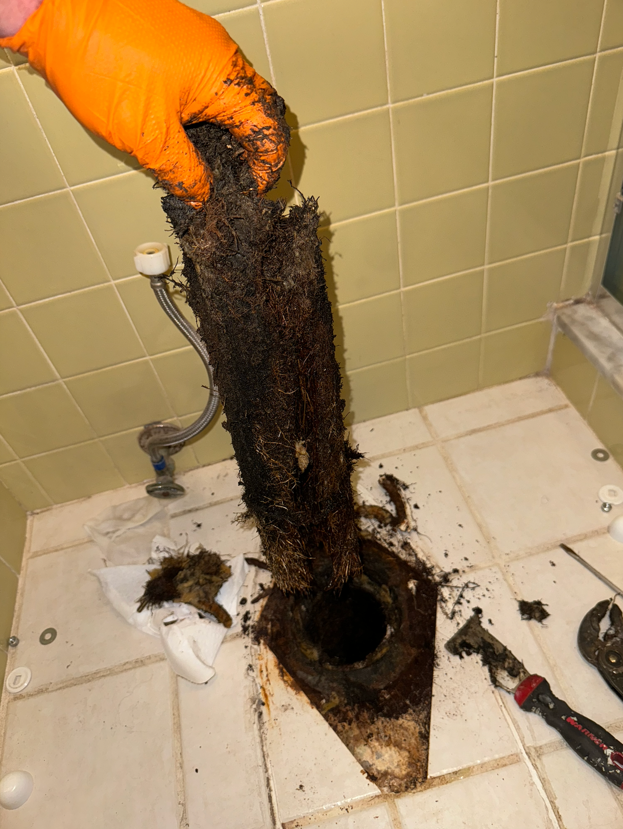 A person wearing orange gloves is cleaning a drain in a bathroom.