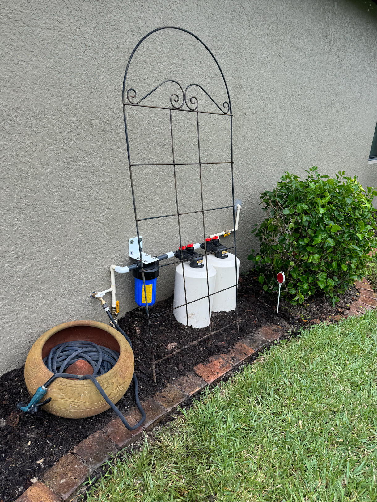 A hose is sitting on the side of a wall next to a trellis.