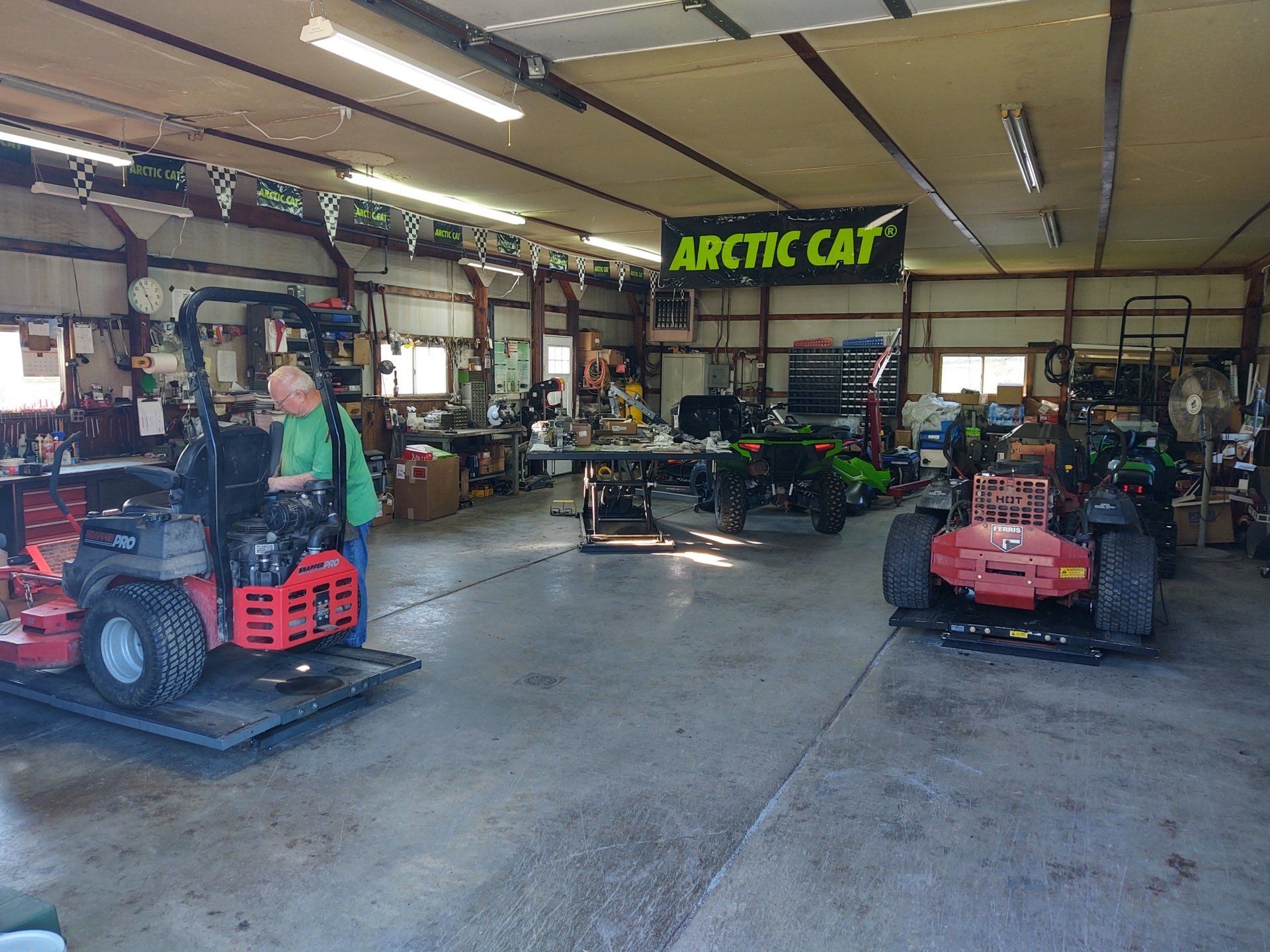 A man is driving a lawn mower in a garage with a sign that says arctic cat