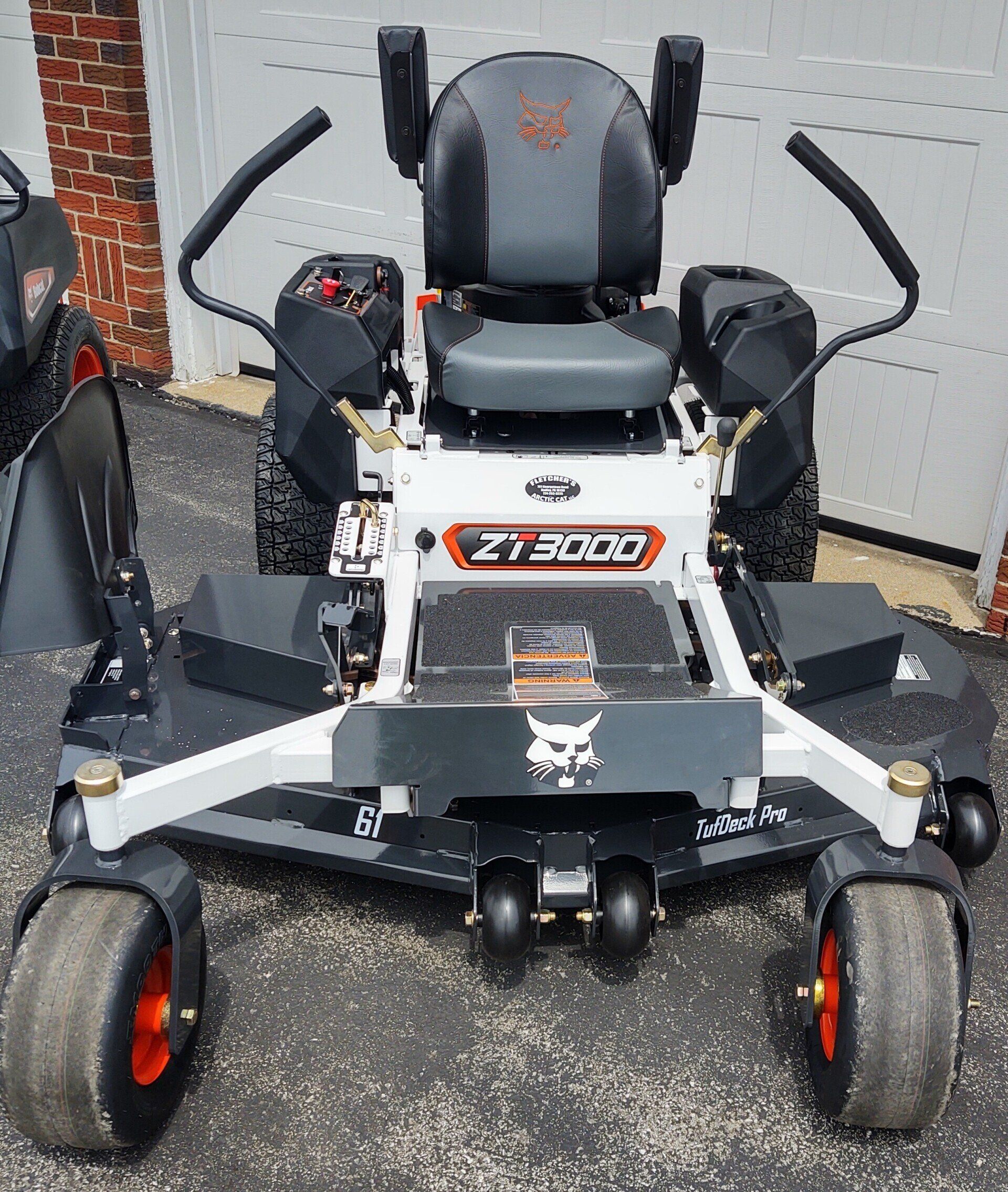 A bobcat zero turn lawn mower is parked in front of a garage.