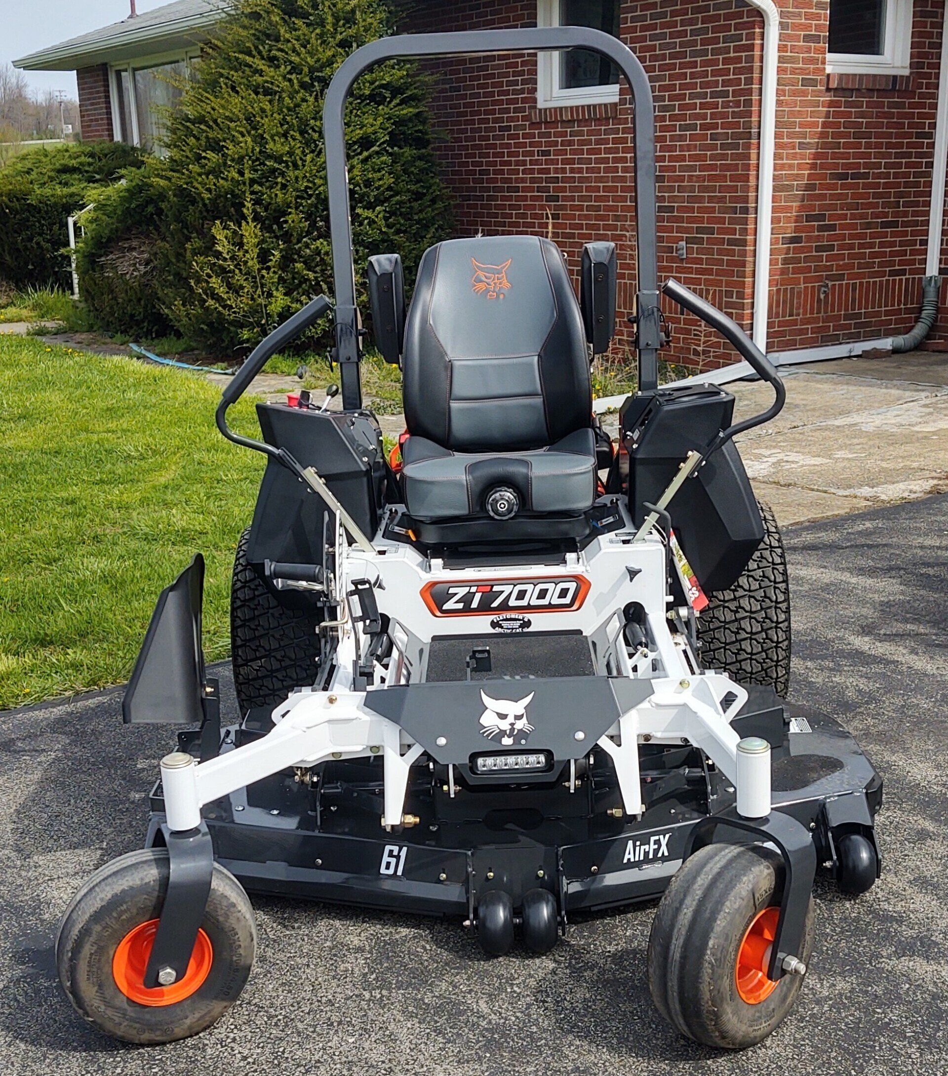 A bobcat zero turn mower is parked in front of a brick house.