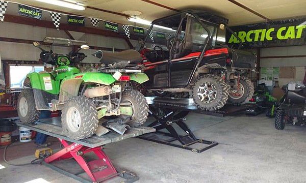 Two atvs are on a lift in a garage with a sign that says arctic cat
