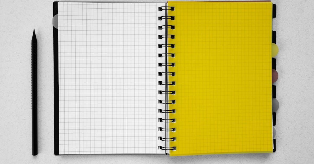 Cahier à spirale ouvert avec papier quadrillé et pages jaunes, crayon noir sur fond blanc.