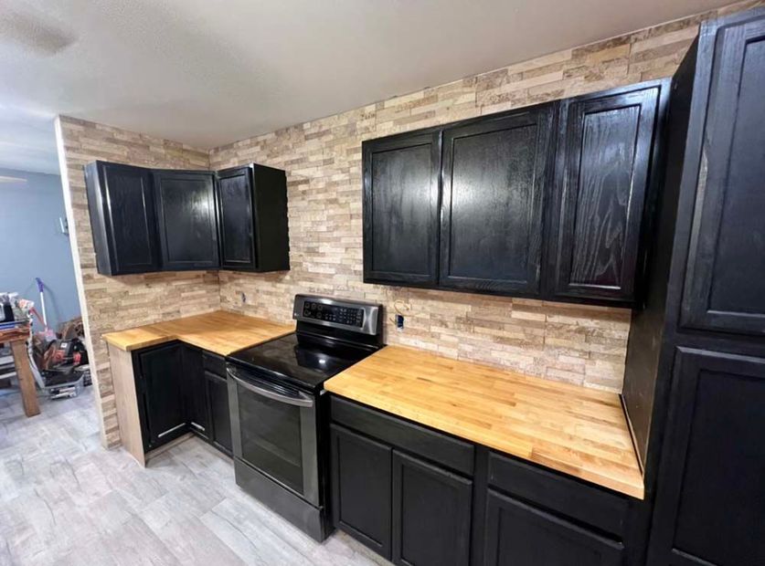 A kitchen with black cabinets and wooden counter tops.