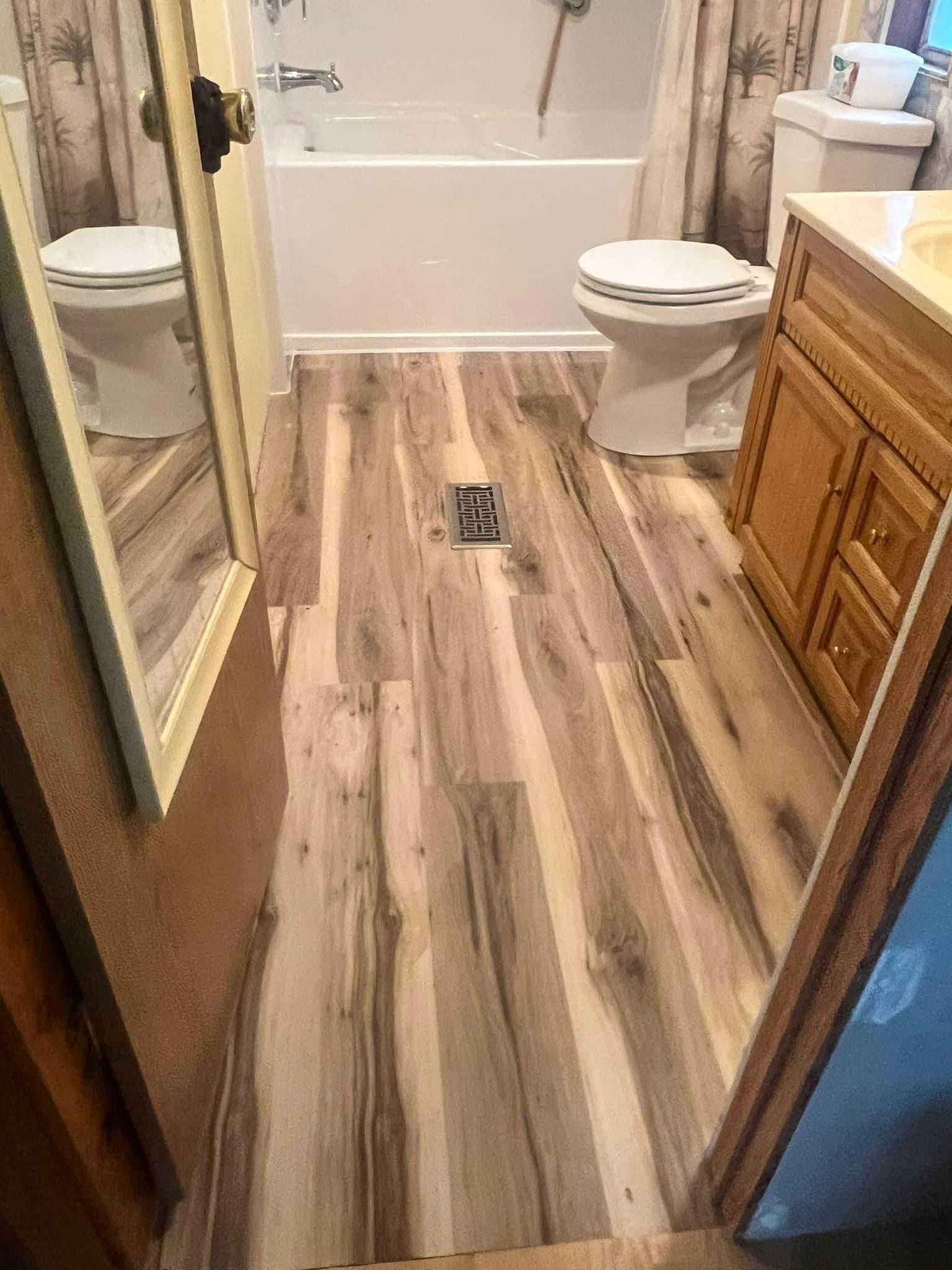 A bathroom with a wooden floor , toilet , sink and bathtub.