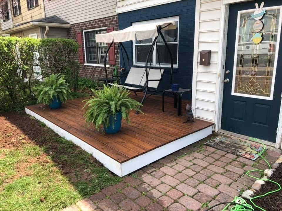 A wooden deck with a swing and potted plants in front of a house.
