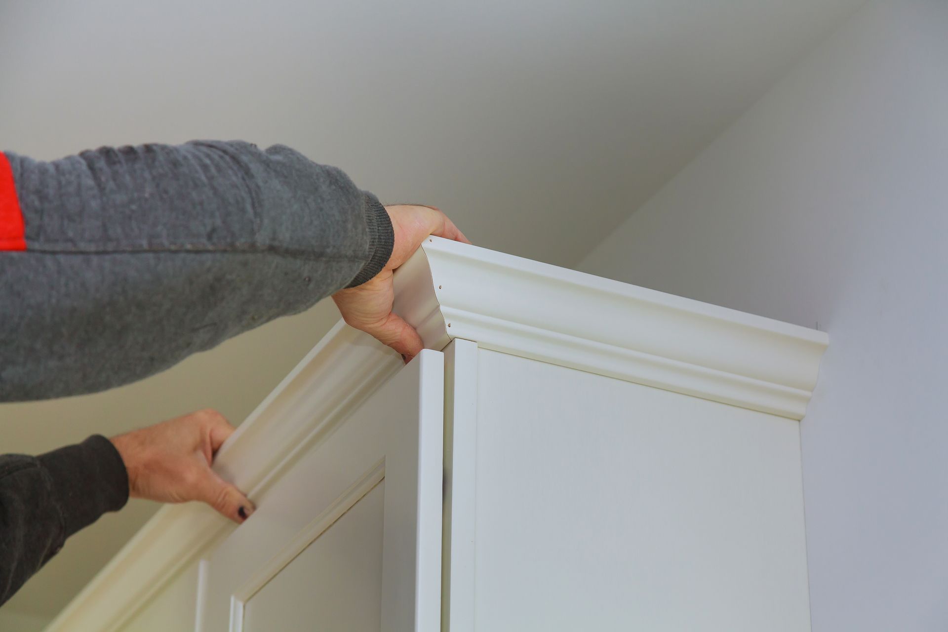 Person installing white crown molding on a white cabinet.