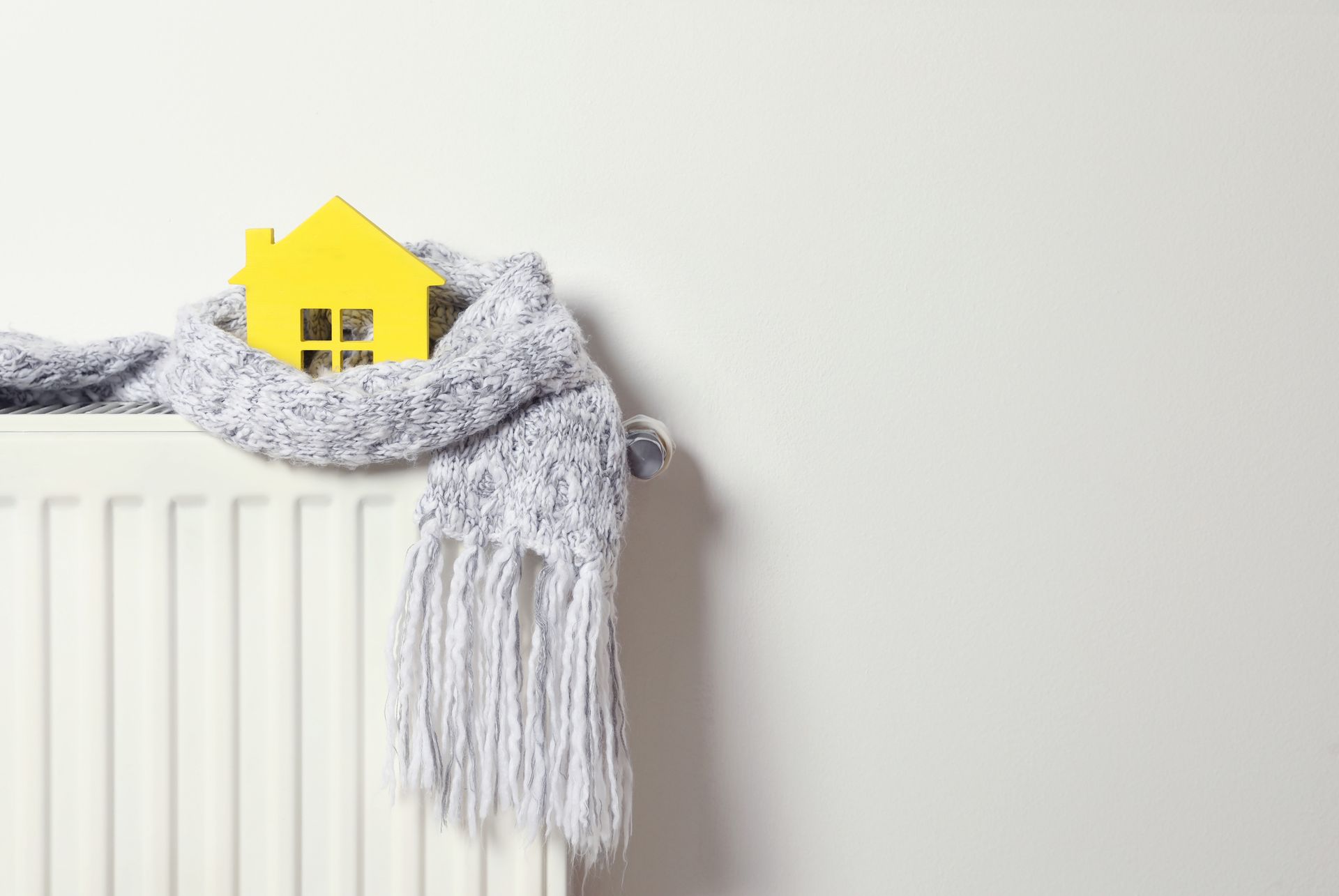 A yellow house is wrapped in a scarf on a radiator. House is warm because of our Utilities deals.
