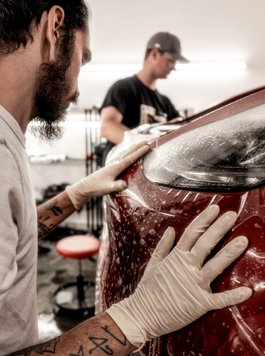 a man is wrapping a red car with plastic wrap .