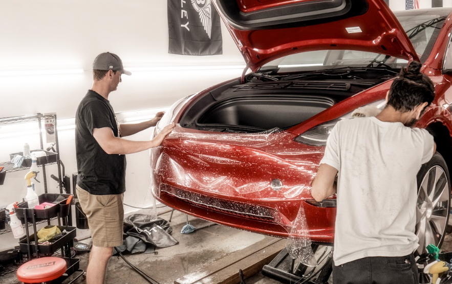 two men are working on a red car in a garage .