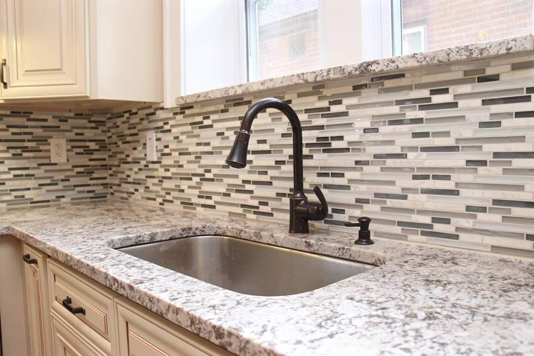 Kitchen countertop with stainless steel sink, black faucet, and mosaic tile backsplash.