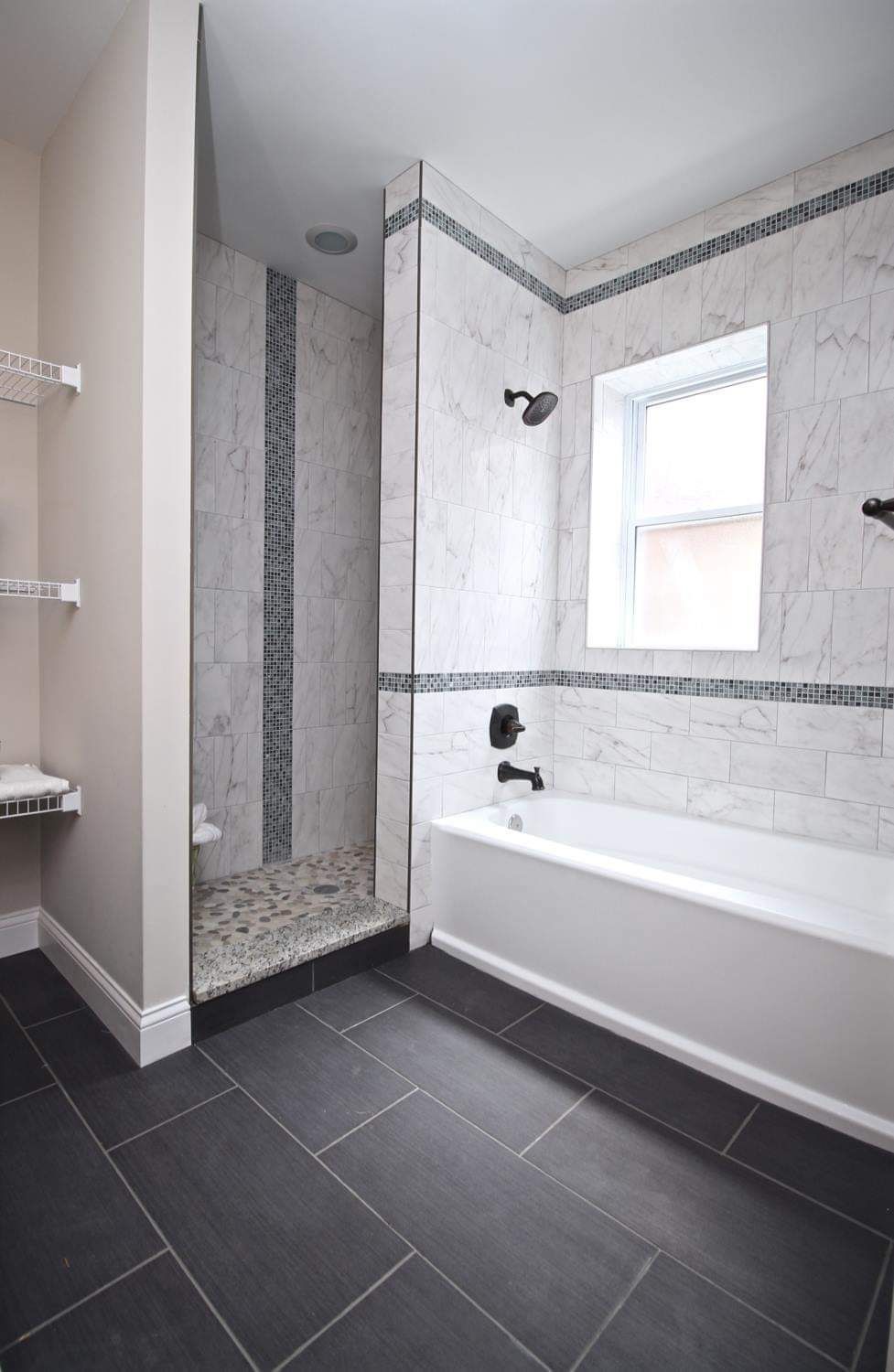 Bathroom with a white bathtub, tiled shower, dark gray floor, and light walls.