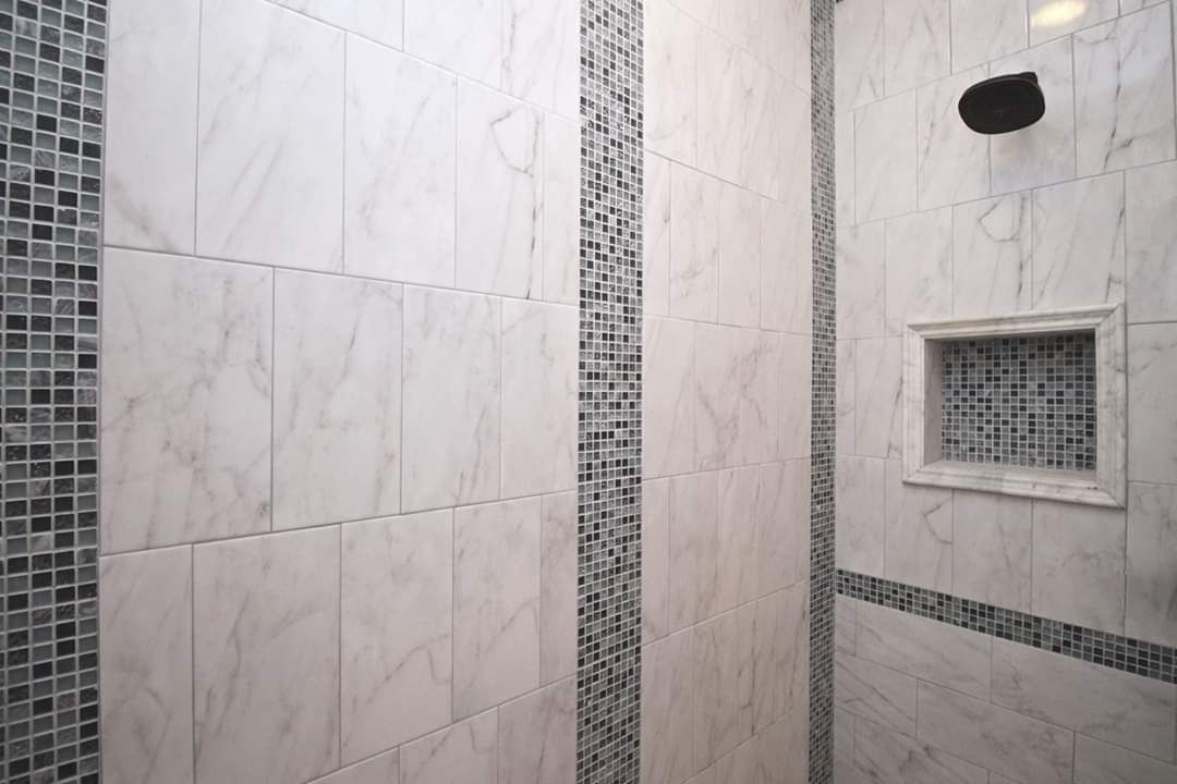 Tiled shower with white marble-like walls and mosaic tile accents. Built-in shelf and showerhead visible.