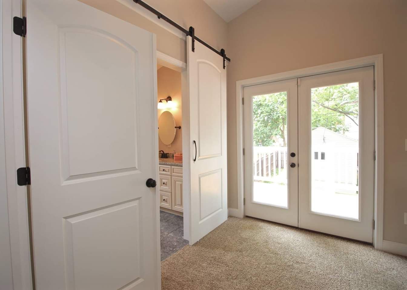 Interior view of a room with a sliding door, bathroom, and French doors leading to a deck.