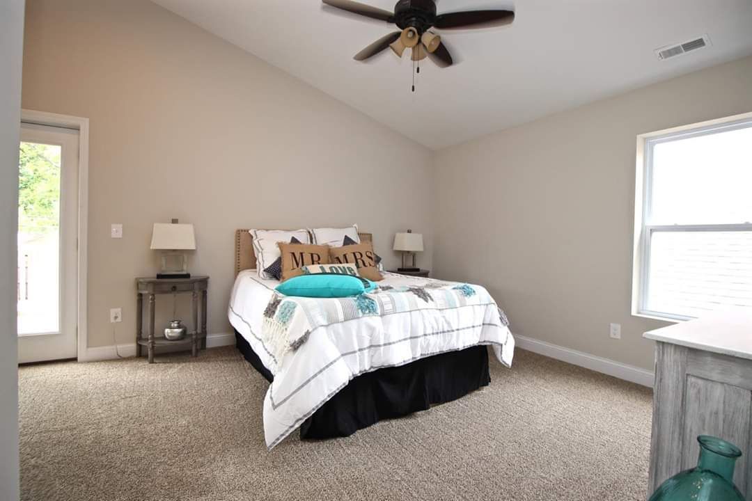Bedroom with bed, nightstands, window, door, beige walls, and brown carpet.