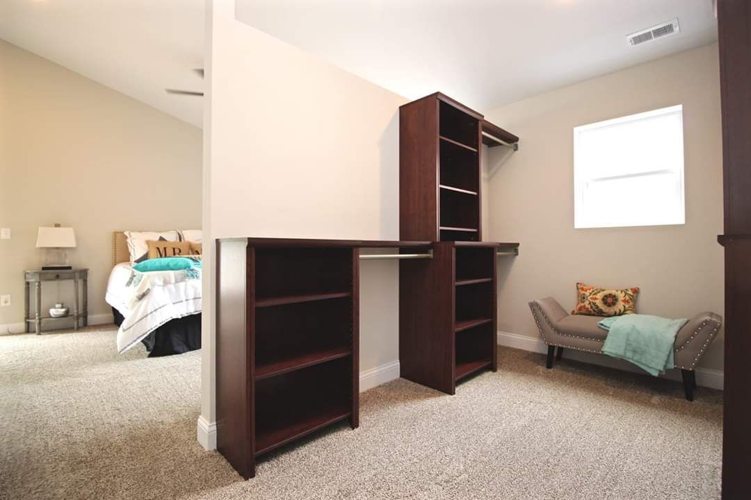 Walk-in closet with dark brown shelving and a bench, next to a bedroom with bed and window.