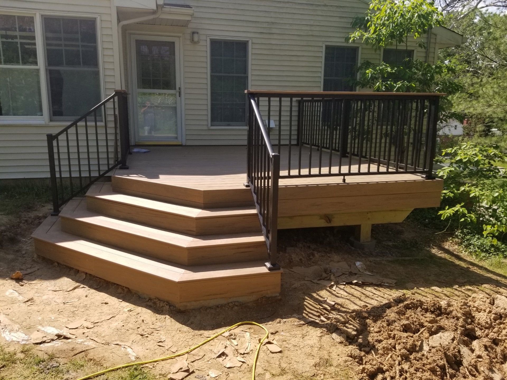 A concrete deck with steps and black railing attached to a beige house, surrounded by dirt.