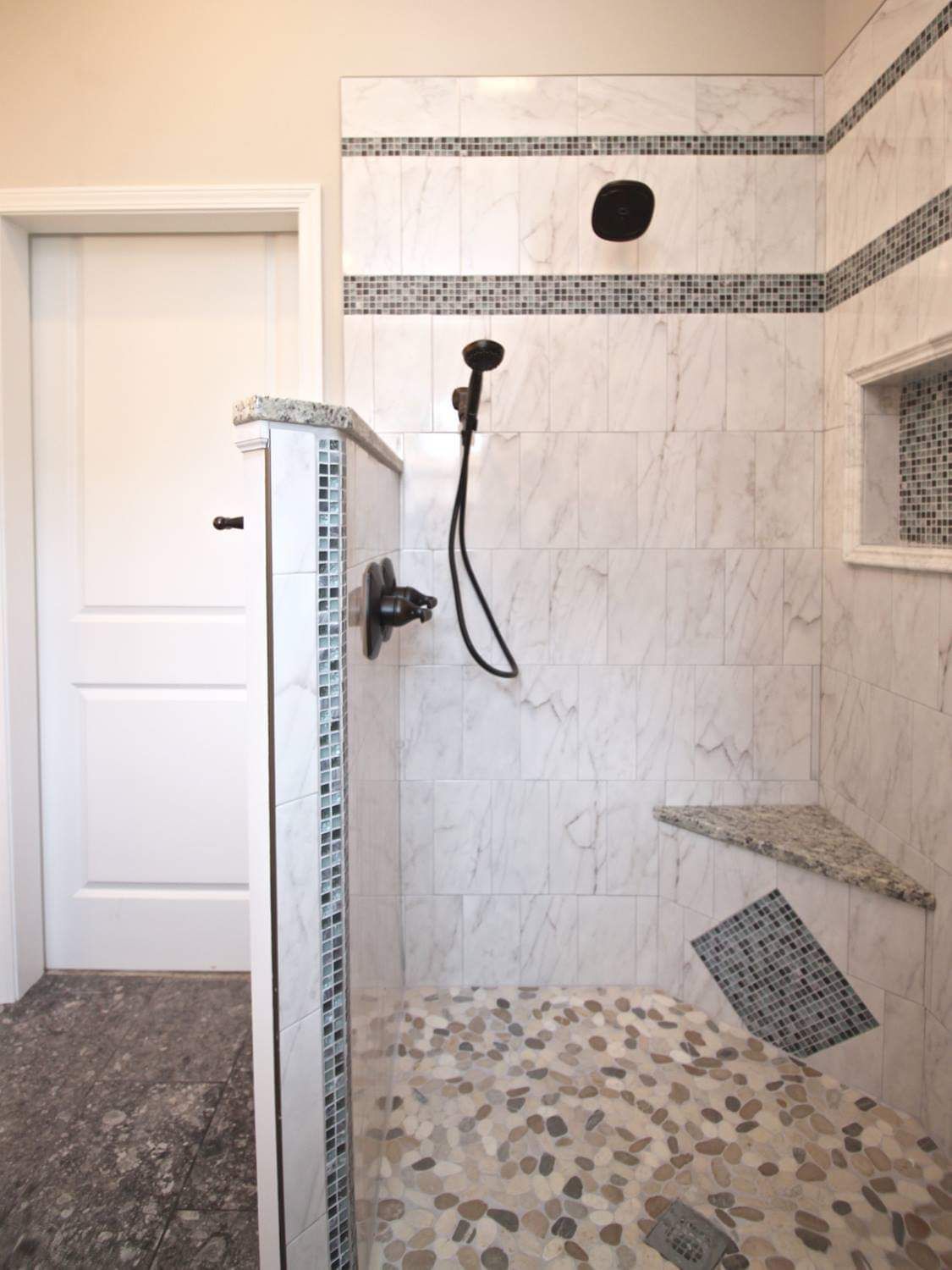 Shower with white marble tiles, pebble floor, mosaic accents, and a built-in bench.