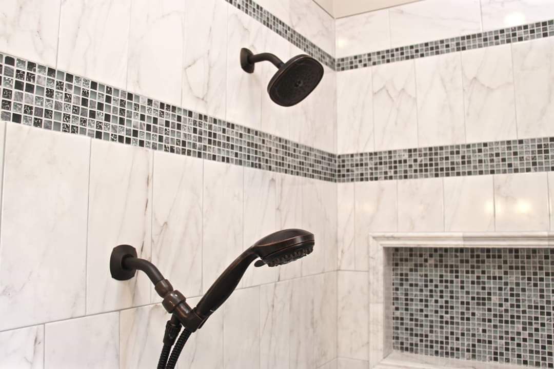 Shower with white marble-look tiles, mosaic tile accent, and two dark showerheads.