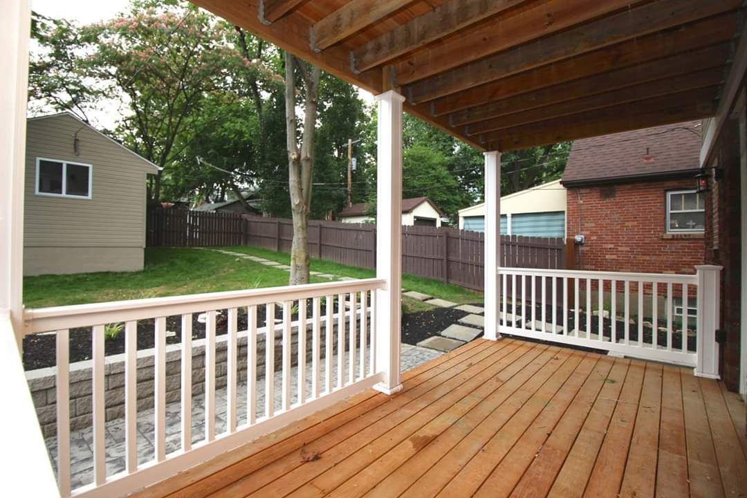 Wooden deck with white railing and support posts, overlooking a backyard with trees and houses.