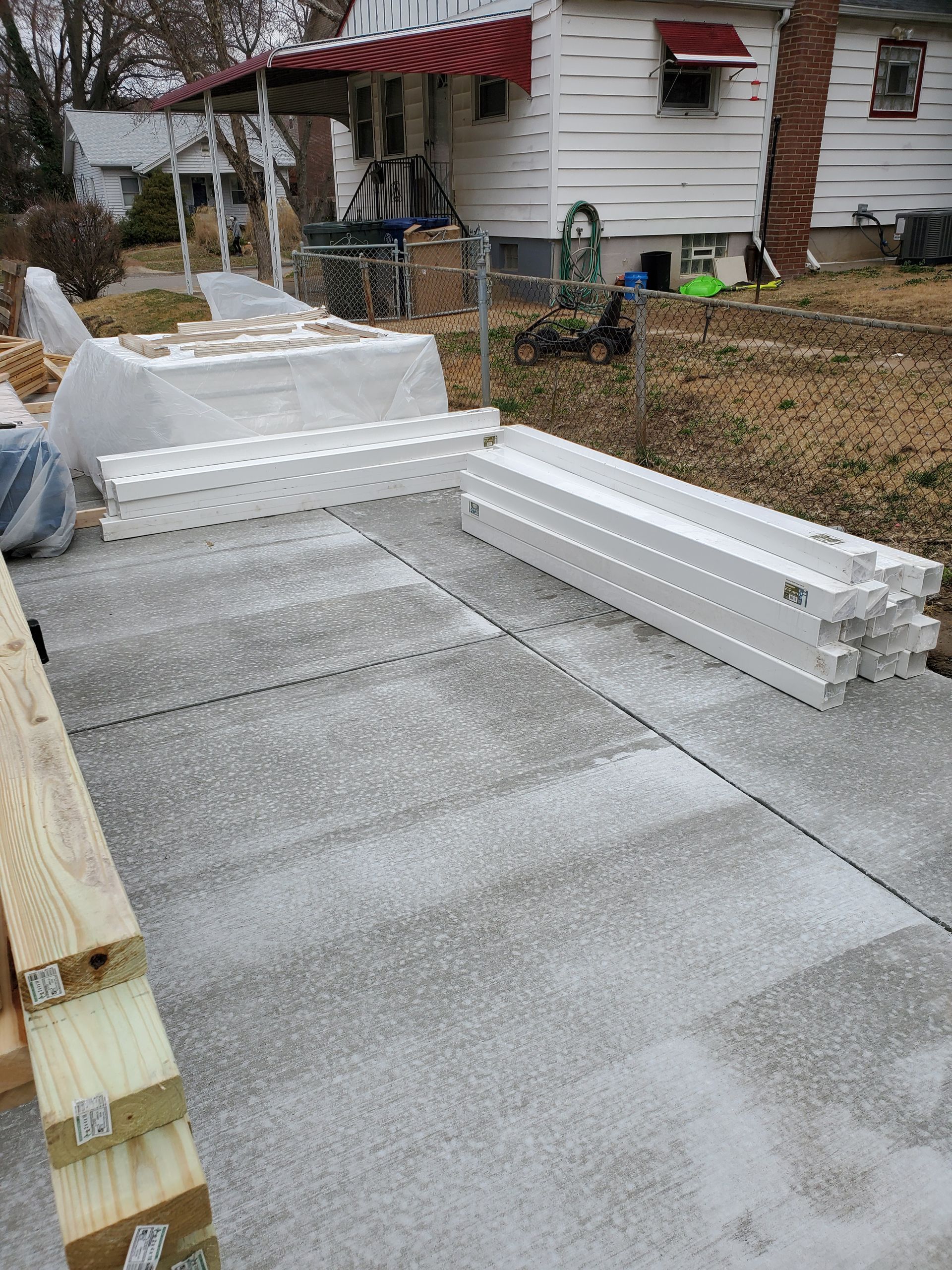 White vinyl posts and wooden beams on a concrete driveway in front of a house.