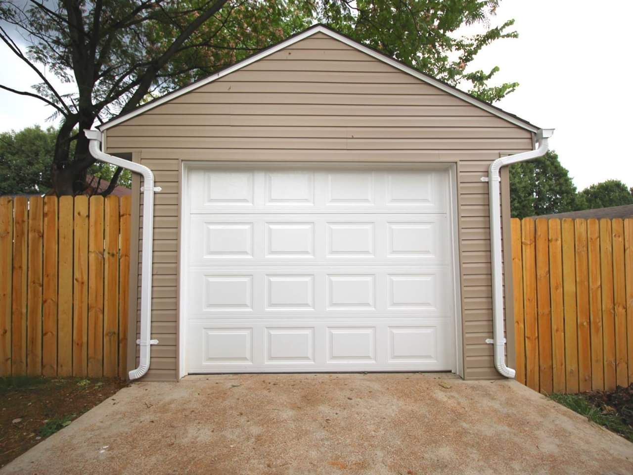 White garage door on tan building, flanked by wooden fence and gutters, on concrete driveway.